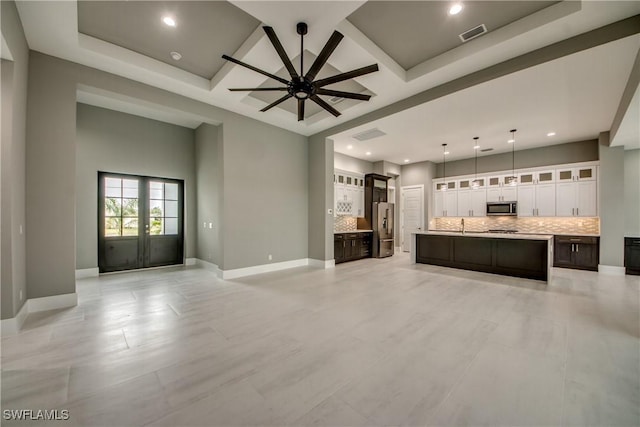 unfurnished living room featuring coffered ceiling, ceiling fan, a towering ceiling, and baseboards