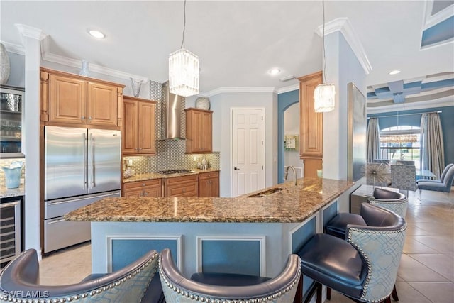 kitchen with arched walkways, wall chimney range hood, gas cooktop, a sink, and built in fridge