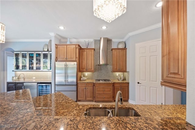 kitchen featuring wine cooler, a sink, appliances with stainless steel finishes, dark stone counters, and wall chimney exhaust hood