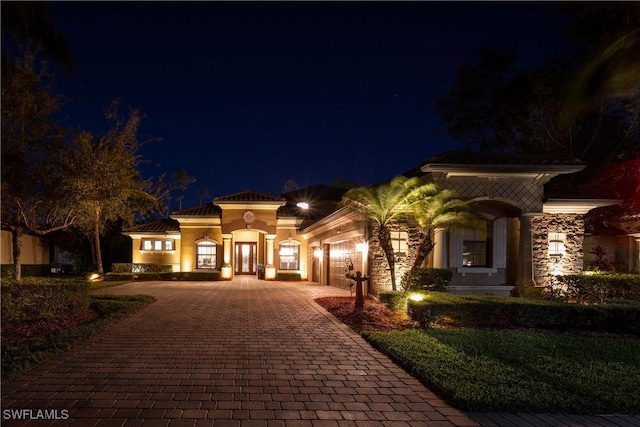 mediterranean / spanish home featuring a garage, decorative driveway, and stone siding