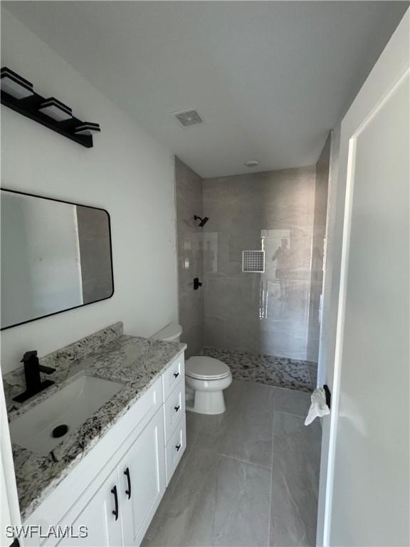 full bath featuring toilet, visible vents, tiled shower, and vanity