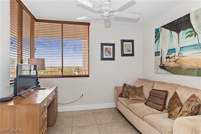 living area featuring light tile patterned floors, a ceiling fan, and baseboards