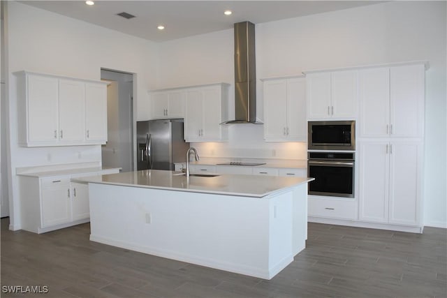 kitchen with a center island with sink, stainless steel appliances, wall chimney range hood, white cabinetry, and a sink