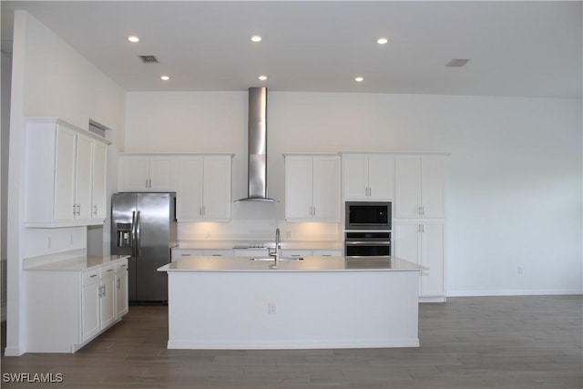 kitchen featuring a center island with sink, visible vents, white cabinets, stainless steel appliances, and wall chimney range hood