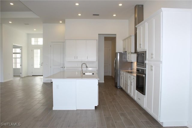 kitchen featuring stainless steel appliances, white cabinetry, a sink, and a center island with sink