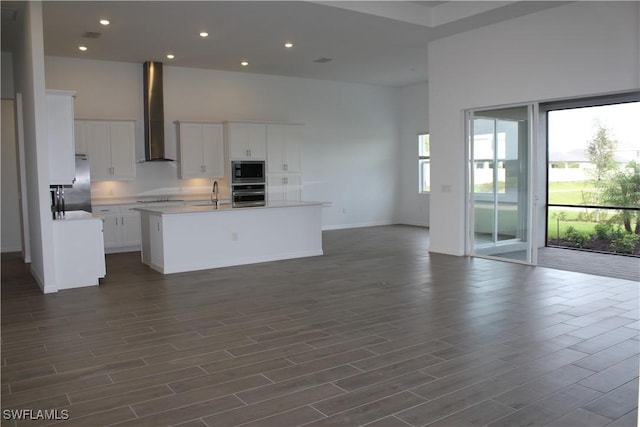 kitchen featuring refrigerator, a towering ceiling, stainless steel oven, built in microwave, and wall chimney exhaust hood