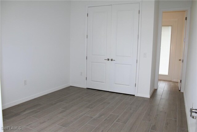 unfurnished bedroom featuring wood finish floors, a closet, and baseboards