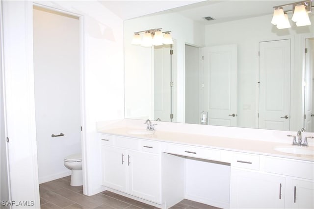 full bath with visible vents, a sink, toilet, and double vanity