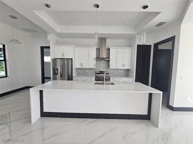 kitchen with visible vents, a tray ceiling, stainless steel appliances, wall chimney exhaust hood, and a sink