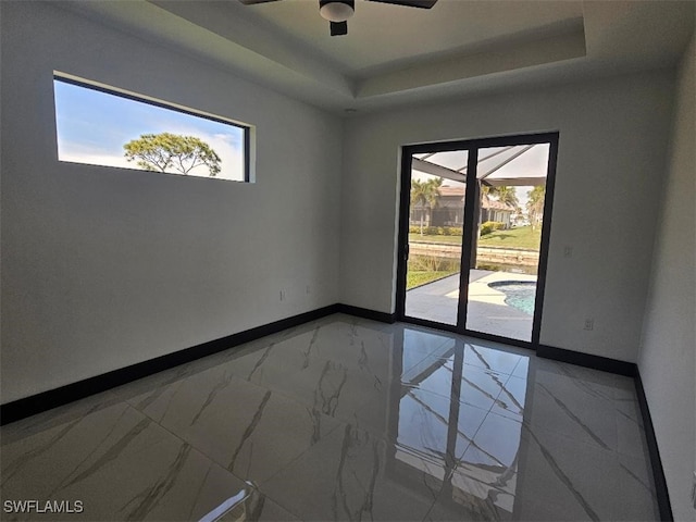 spare room with a tray ceiling, plenty of natural light, baseboards, and marble finish floor