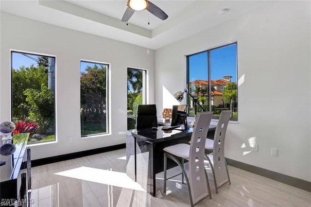 office space featuring a raised ceiling, baseboards, and ceiling fan