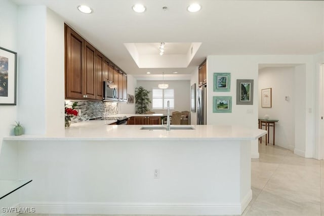 kitchen with a tray ceiling, stainless steel appliances, a sink, and light countertops