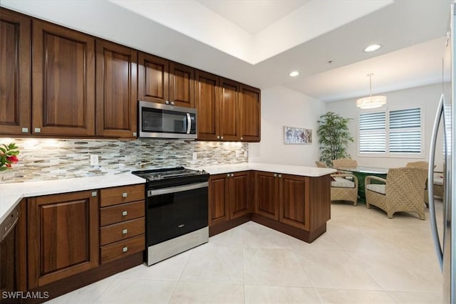 kitchen with appliances with stainless steel finishes, light countertops, a peninsula, and decorative backsplash