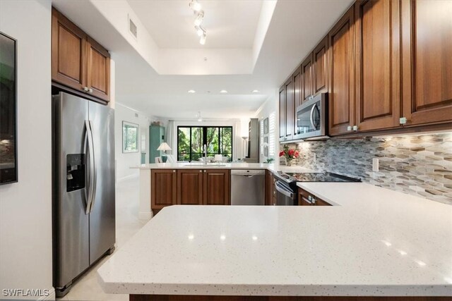 kitchen featuring stainless steel appliances, a peninsula, visible vents, decorative backsplash, and a raised ceiling