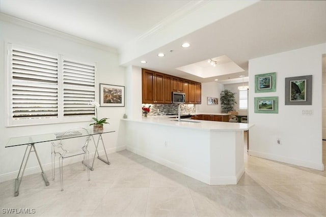 kitchen featuring crown molding, stainless steel microwave, backsplash, brown cabinetry, and a peninsula