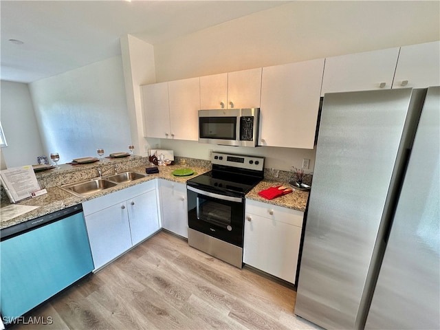 kitchen featuring white cabinets, light stone counters, stainless steel appliances, light wood-type flooring, and a sink