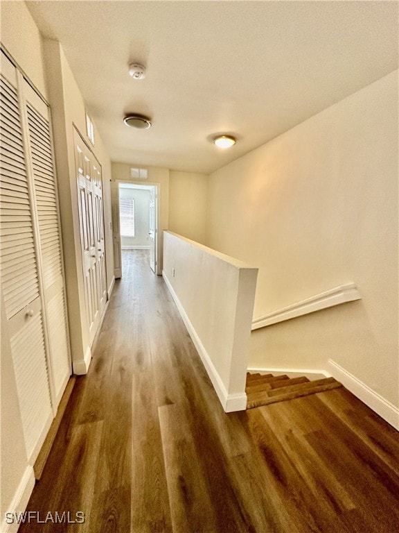 hallway with dark wood-type flooring, baseboards, and an upstairs landing