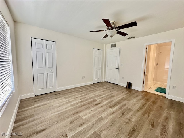 unfurnished bedroom featuring light wood finished floors, two closets, and visible vents