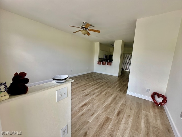 empty room featuring light wood-type flooring, a ceiling fan, and baseboards