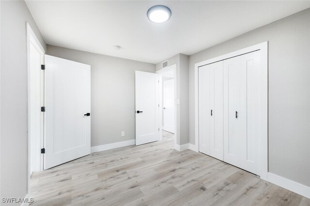 unfurnished bedroom featuring a closet, baseboards, visible vents, and light wood finished floors