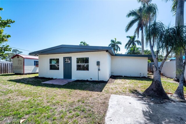 rear view of property featuring stucco siding, fence, an outbuilding, and a yard