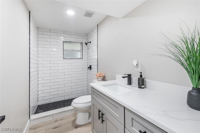 full bath with visible vents, toilet, vanity, wood finished floors, and tiled shower