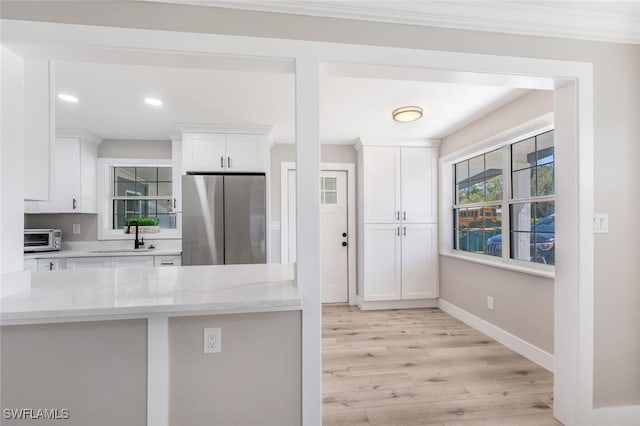 kitchen with a toaster, freestanding refrigerator, white cabinetry, a sink, and light wood-type flooring