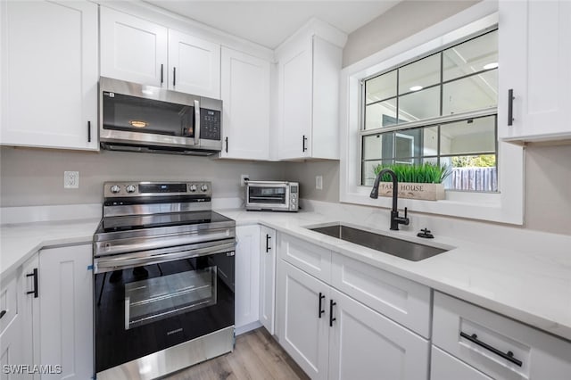 kitchen featuring a toaster, appliances with stainless steel finishes, light wood-style floors, white cabinets, and a sink