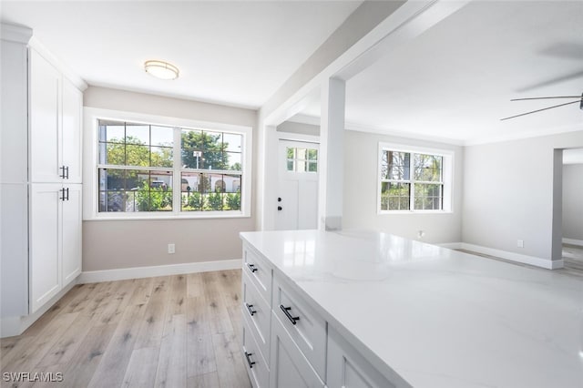 kitchen featuring baseboards, ceiling fan, light stone counters, light wood-style floors, and white cabinetry