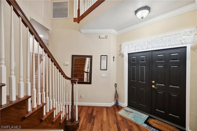 entryway featuring visible vents, baseboards, crown molding, stairway, and wood finished floors
