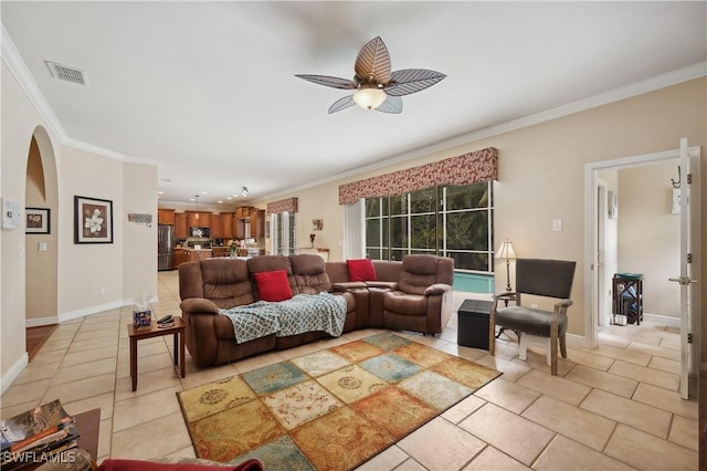 living area with crown molding, arched walkways, a ceiling fan, visible vents, and baseboards