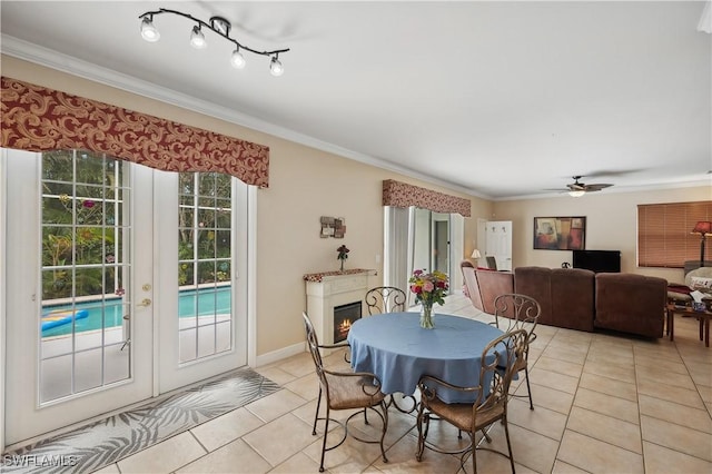 dining area featuring ceiling fan, crown molding, a warm lit fireplace, and light tile patterned flooring