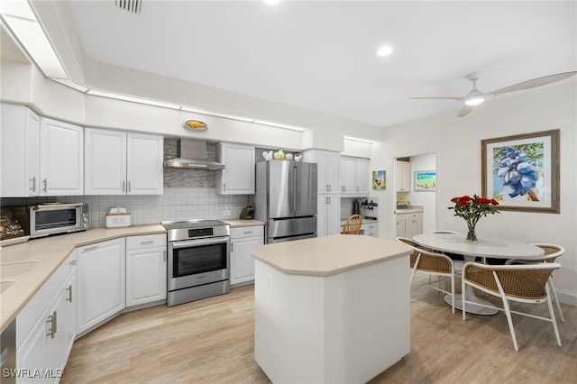 kitchen with a toaster, stainless steel appliances, light wood-style flooring, decorative backsplash, and wall chimney range hood