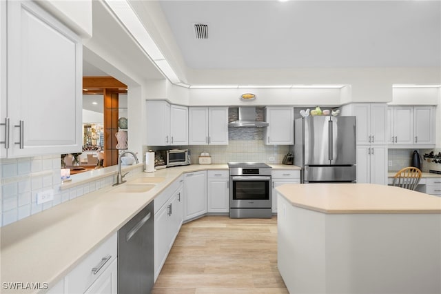 kitchen with light wood finished floors, backsplash, appliances with stainless steel finishes, a sink, and wall chimney range hood