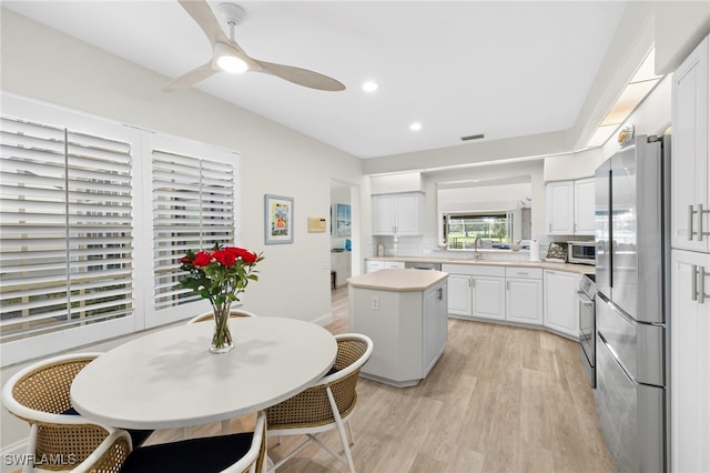 kitchen with stainless steel appliances, light countertops, backsplash, white cabinetry, and light wood-type flooring