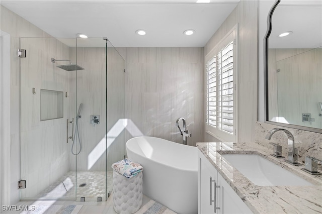 full bathroom with tile walls, recessed lighting, a shower stall, vanity, and a freestanding tub