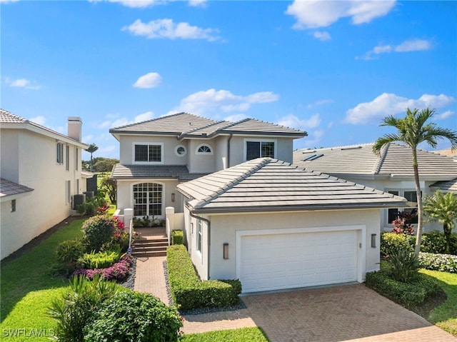 view of front facade featuring a garage, a tiled roof, decorative driveway, central AC, and stucco siding