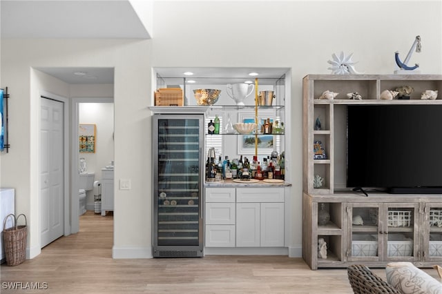 bar with a dry bar, light wood-style floors, wine cooler, and baseboards