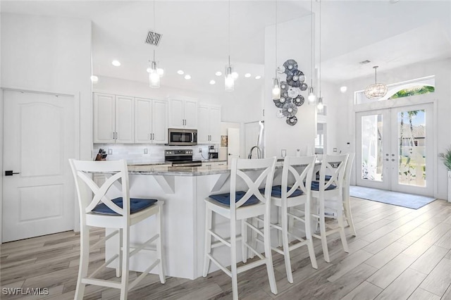 kitchen featuring appliances with stainless steel finishes, french doors, light wood-style floors, white cabinetry, and backsplash