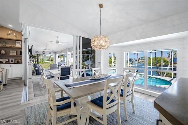 dining space with light wood-type flooring, a wealth of natural light, vaulted ceiling, and an inviting chandelier