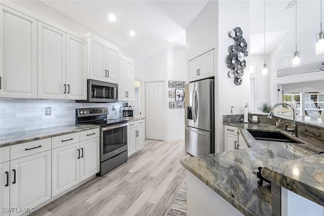 kitchen featuring tasteful backsplash, dark stone counters, stainless steel appliances, white cabinetry, and a sink