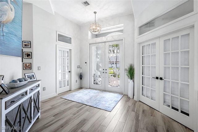 foyer with baseboards, visible vents, french doors, light wood-type flooring, and a notable chandelier