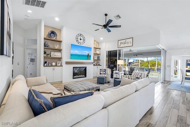 living room featuring a ceiling fan, a fireplace, visible vents, and wood finished floors