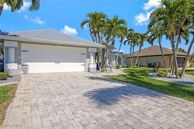 single story home featuring decorative driveway, metal roof, an attached garage, and stucco siding