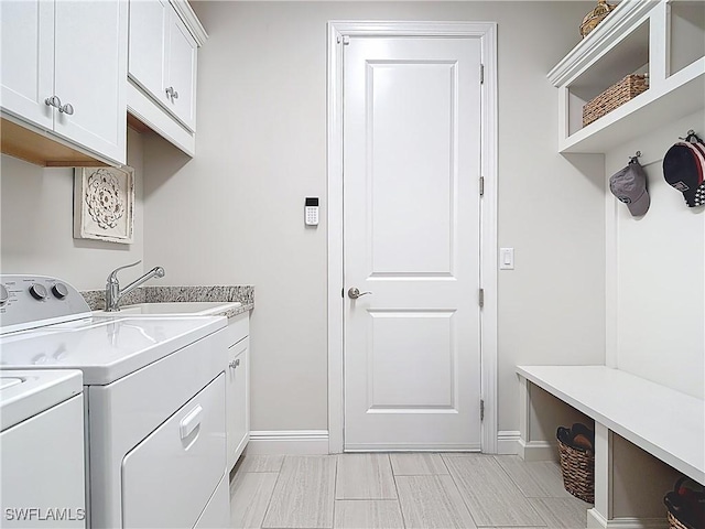 clothes washing area featuring independent washer and dryer, cabinet space, a sink, and baseboards