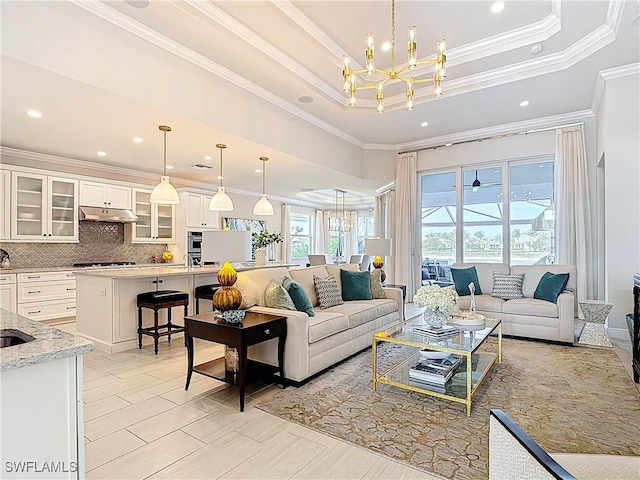 living room with ornamental molding, a tray ceiling, recessed lighting, and an inviting chandelier