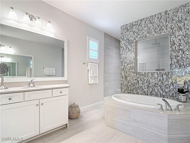 bathroom with a garden tub, baseboards, tiled shower, and vanity