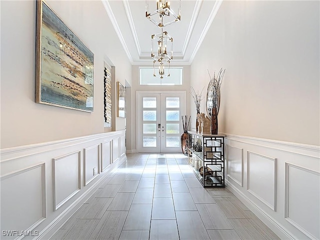 foyer entrance with a chandelier, french doors, crown molding, and a decorative wall