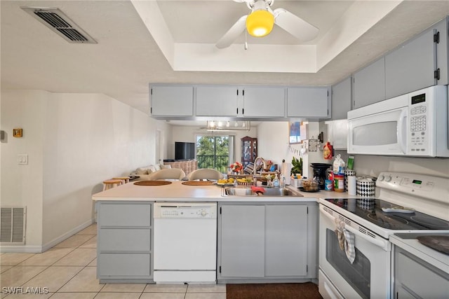 kitchen with a peninsula, white appliances, a sink, and visible vents