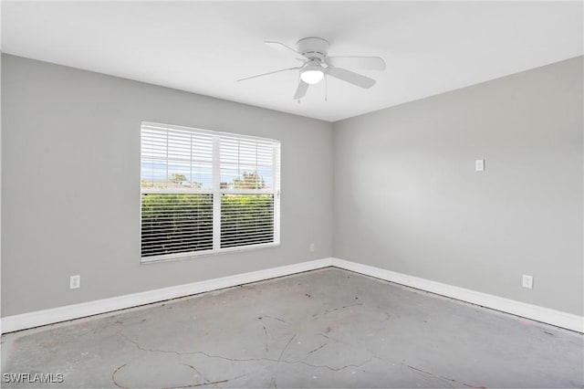 spare room featuring unfinished concrete floors, baseboards, and a ceiling fan